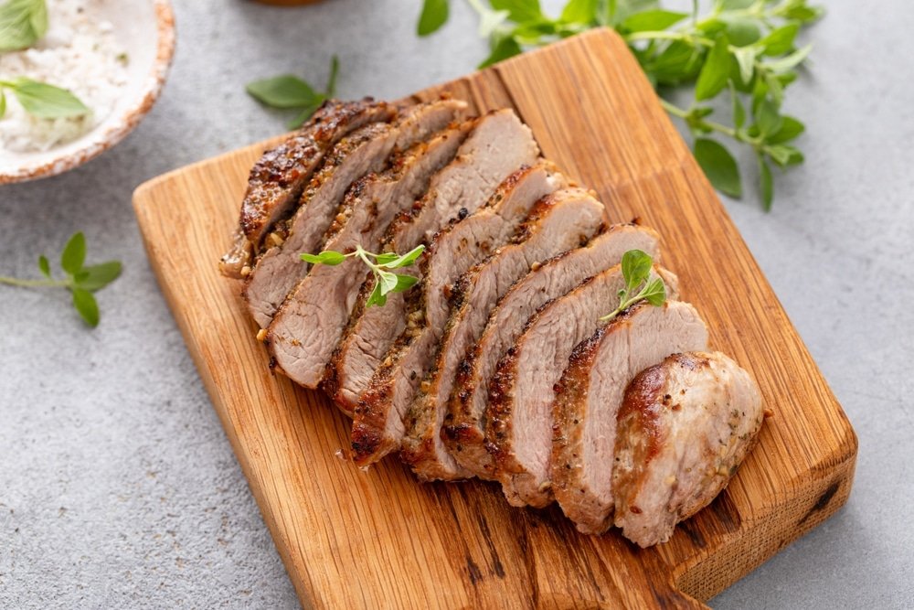 Grilled,Pork,Chop,Sliced,On,A,Cutting,Board,With,Herbs